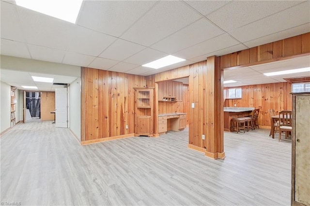 basement with wood walls, a paneled ceiling, and light hardwood / wood-style floors