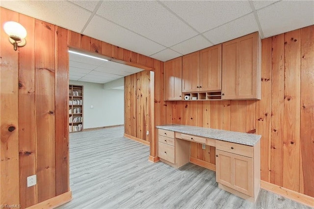 kitchen featuring wood walls, built in desk, light hardwood / wood-style floors, and a drop ceiling