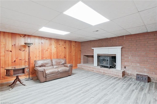 living room featuring wood walls, a drop ceiling, brick wall, light wood-type flooring, and a fireplace