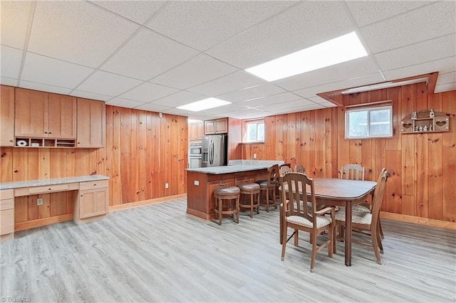 dining space with wood walls, a paneled ceiling, and light wood-type flooring