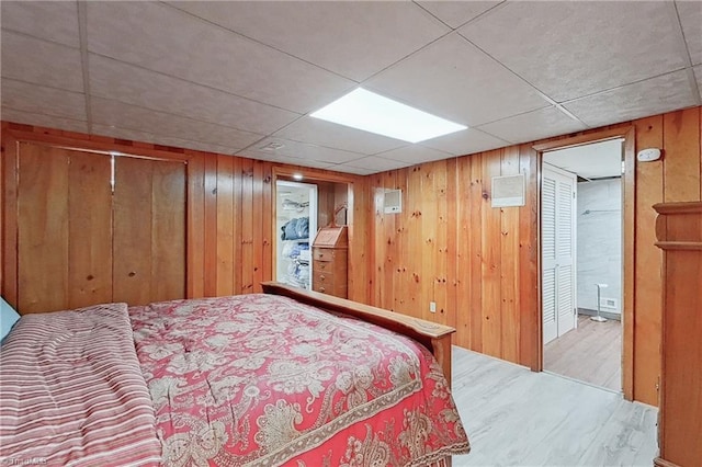 bedroom featuring a paneled ceiling, wooden walls, and light hardwood / wood-style flooring