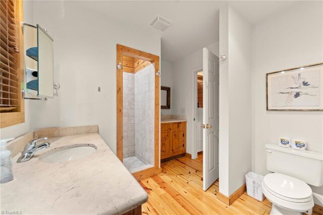 bathroom with vanity, a tile shower, wood-type flooring, and toilet