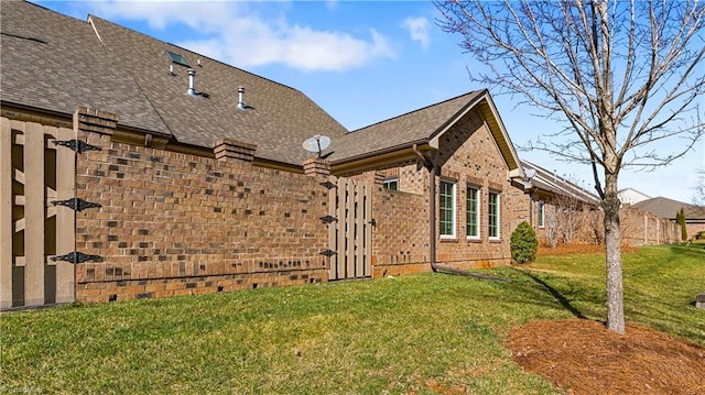 view of home's exterior featuring brick siding, a lawn, a shingled roof, and fence