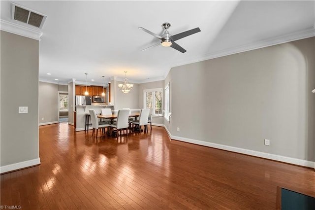 dining room featuring ceiling fan with notable chandelier, visible vents, baseboards, ornamental molding, and dark wood-style floors