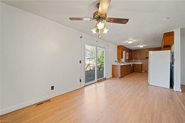 unfurnished living room with light wood-type flooring, visible vents, baseboards, and a ceiling fan