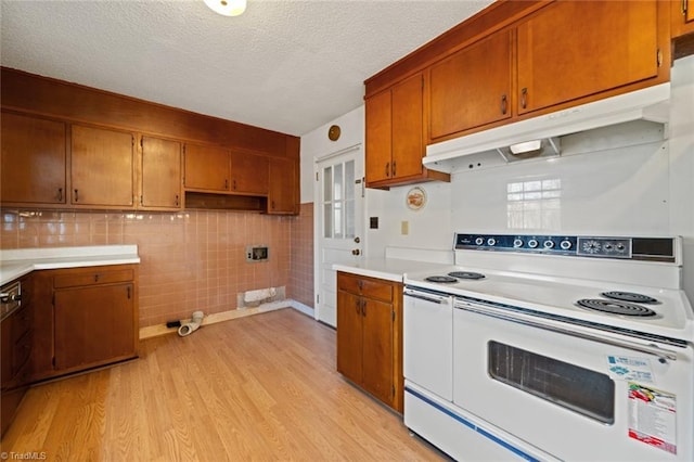 kitchen with under cabinet range hood, light wood finished floors, brown cabinetry, and white electric range oven