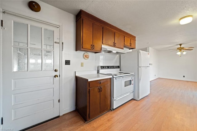 kitchen with light wood-type flooring, brown cabinets, under cabinet range hood, a textured ceiling, and white appliances