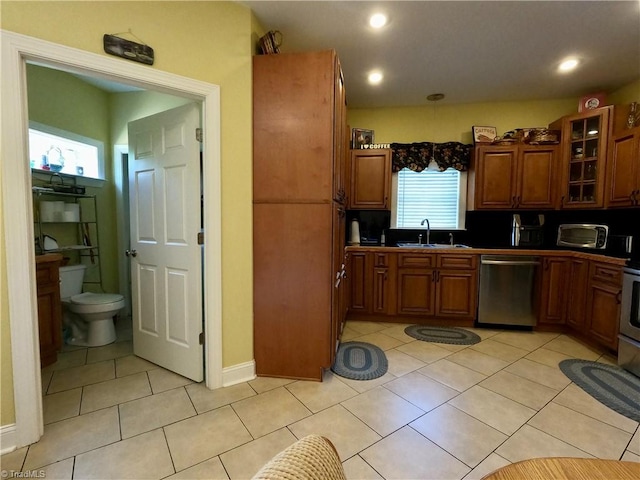 kitchen featuring stainless steel dishwasher, a sink, brown cabinets, glass insert cabinets, and light tile patterned floors