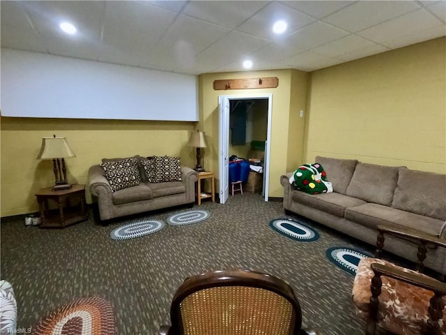 carpeted living area featuring a drop ceiling and concrete block wall