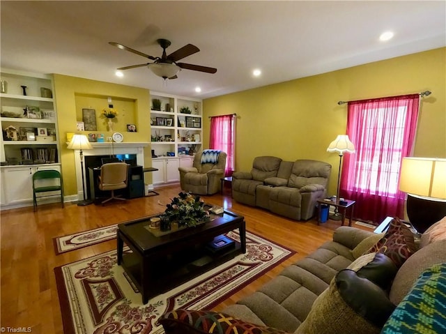 living area with a fireplace with flush hearth, ceiling fan, wood finished floors, built in shelves, and recessed lighting