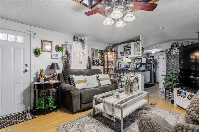 living room with lofted ceiling, hardwood / wood-style floors, a textured ceiling, and ceiling fan