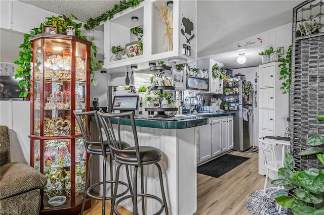 kitchen featuring a textured ceiling, white cabinets, a kitchen breakfast bar, and light hardwood / wood-style flooring