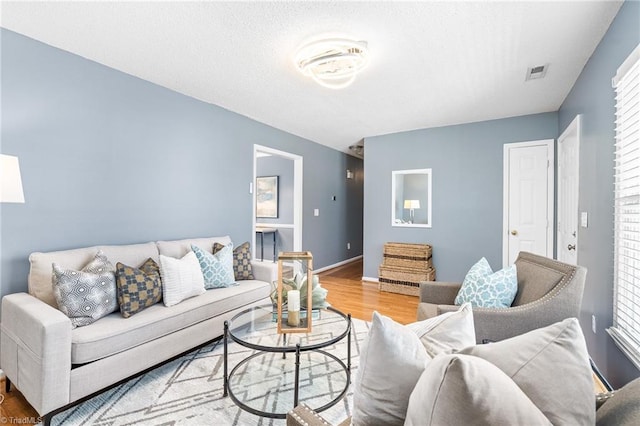 living room featuring visible vents, a textured ceiling, baseboards, and wood finished floors