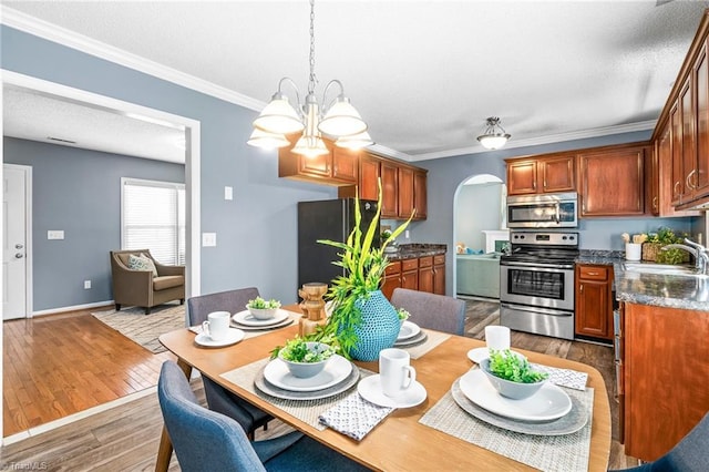 dining area with baseboards, arched walkways, ornamental molding, wood finished floors, and an inviting chandelier