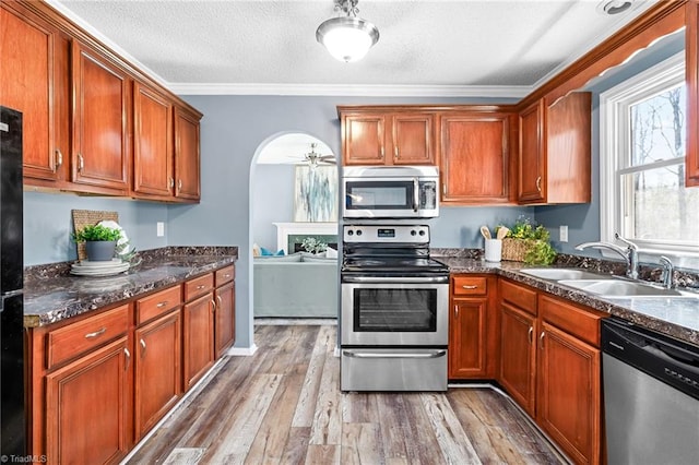 kitchen with arched walkways, appliances with stainless steel finishes, a textured ceiling, light wood-style floors, and a sink