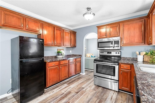 kitchen with arched walkways, crown molding, stainless steel appliances, brown cabinetry, and light wood-type flooring