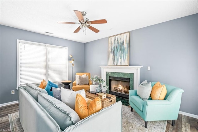 living area with baseboards, visible vents, ceiling fan, wood finished floors, and a high end fireplace