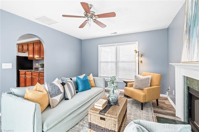 living area featuring arched walkways, a fireplace, wood finished floors, visible vents, and a ceiling fan