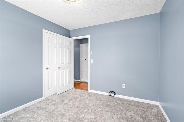 unfurnished bedroom with carpet flooring, a textured ceiling, and baseboards