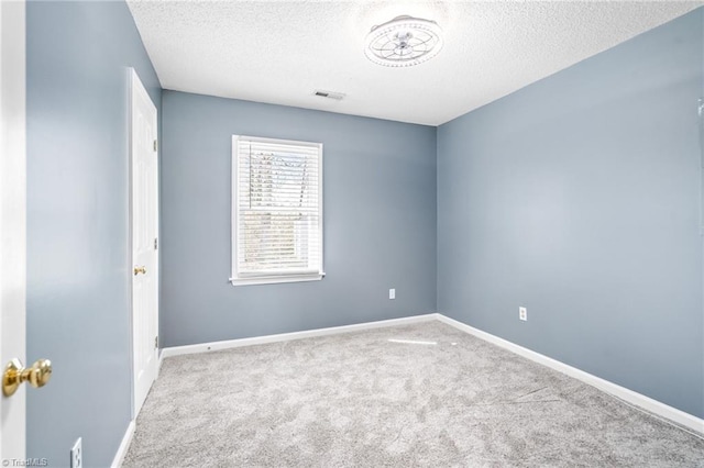 spare room with carpet floors, visible vents, a textured ceiling, and baseboards