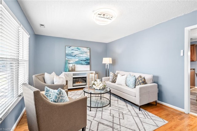 living room featuring baseboards, visible vents, a glass covered fireplace, wood finished floors, and a textured ceiling