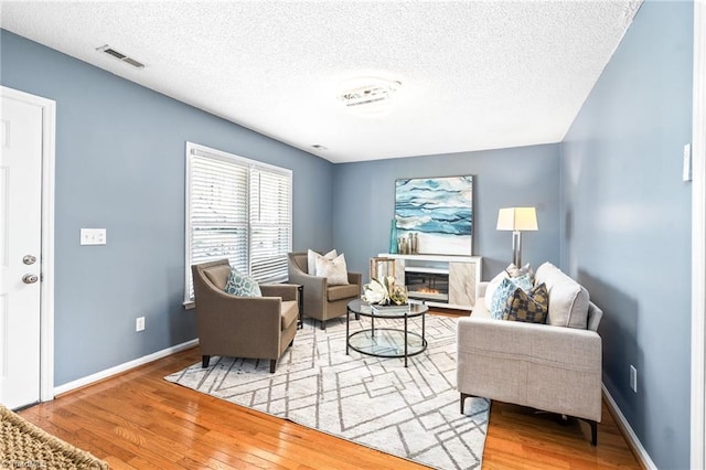 living room with a glass covered fireplace, visible vents, baseboards, and hardwood / wood-style flooring