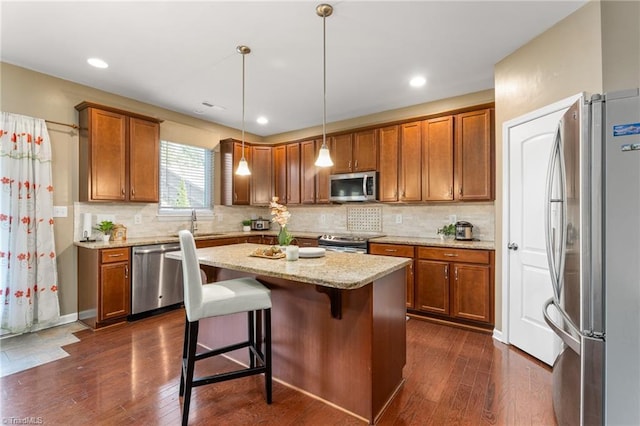 kitchen with brown cabinetry, stainless steel appliances, dark wood finished floors, and a center island