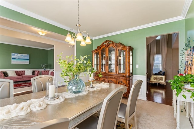 dining space featuring a wainscoted wall, ornamental molding, carpet flooring, and an inviting chandelier