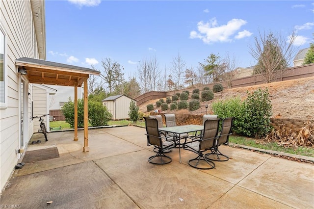 view of patio featuring outdoor dining space, a fenced backyard, an outbuilding, and a storage unit