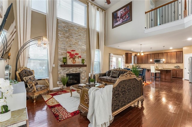 living room with a high ceiling, a ceiling fan, dark wood-type flooring, and a stone fireplace