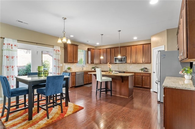 kitchen with dark wood-style flooring, visible vents, backsplash, appliances with stainless steel finishes, and a kitchen island