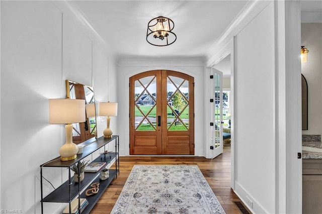 foyer entrance with dark hardwood / wood-style flooring, french doors, an inviting chandelier, and ornamental molding