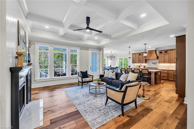 living room with coffered ceiling, ceiling fan with notable chandelier, beam ceiling, hardwood / wood-style flooring, and a premium fireplace