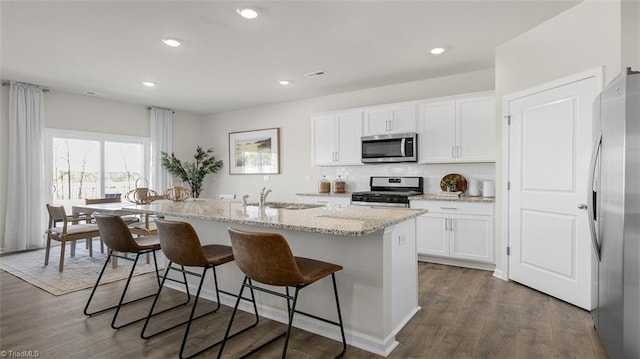 kitchen with stainless steel appliances, white cabinetry, sink, and a center island with sink