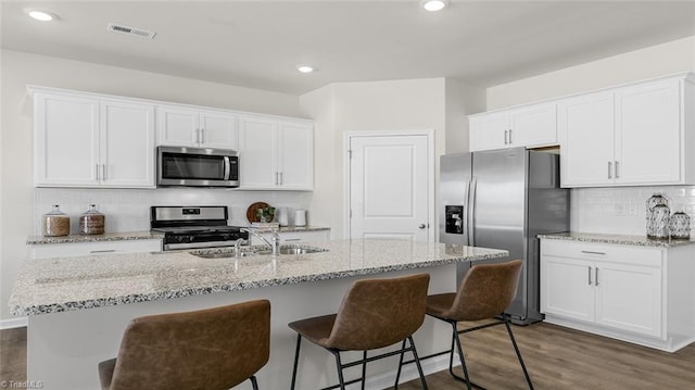 kitchen with light stone counters, an island with sink, white cabinets, and appliances with stainless steel finishes