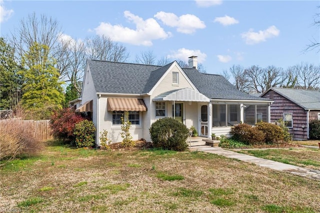 bungalow-style home featuring a shingled roof, a front lawn, a chimney, and a sunroom