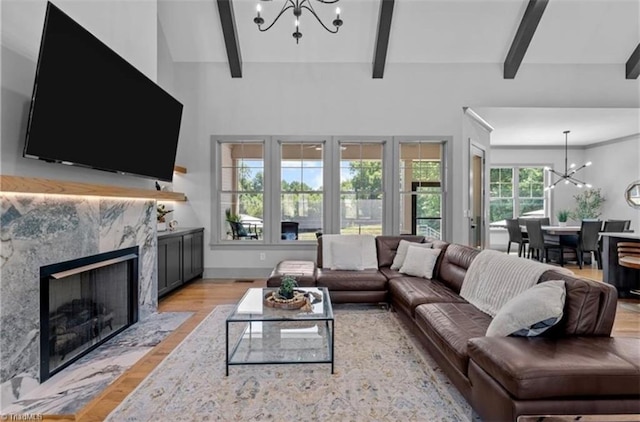 living room featuring a premium fireplace, vaulted ceiling with beams, a chandelier, and light hardwood / wood-style flooring