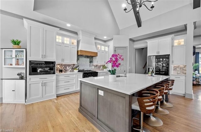 kitchen with white cabinetry, a kitchen island with sink, and premium range hood