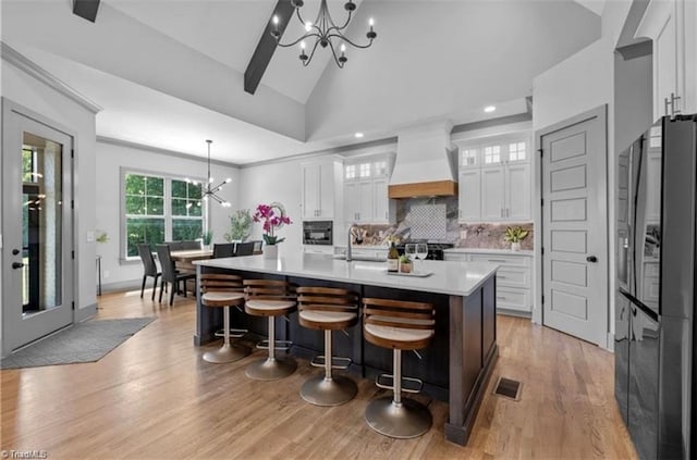 kitchen with pendant lighting, an inviting chandelier, white cabinets, a center island with sink, and custom exhaust hood