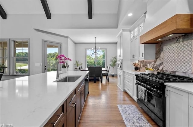 kitchen with black range with gas cooktop, sink, decorative light fixtures, and white cabinetry