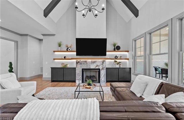 living room with high vaulted ceiling, a chandelier, a high end fireplace, and light hardwood / wood-style flooring