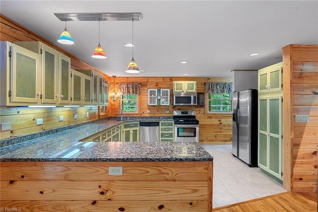 kitchen with wood walls, a peninsula, glass insert cabinets, hanging light fixtures, and stainless steel appliances