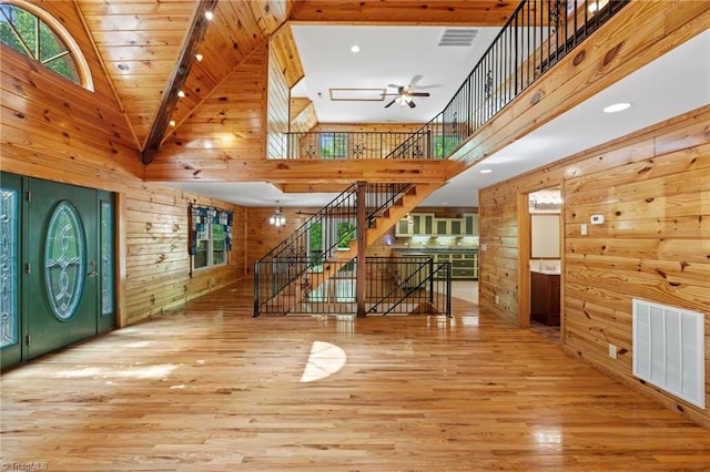 foyer with visible vents, wood finished floors, ceiling fan, a high ceiling, and wooden walls