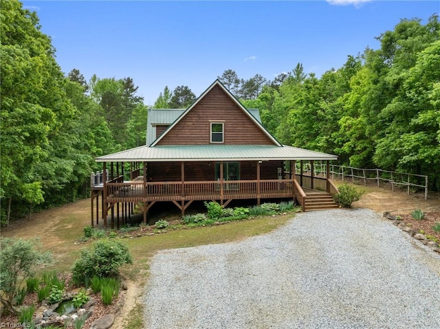 farmhouse-style home featuring fence, a view of trees, covered porch, and metal roof