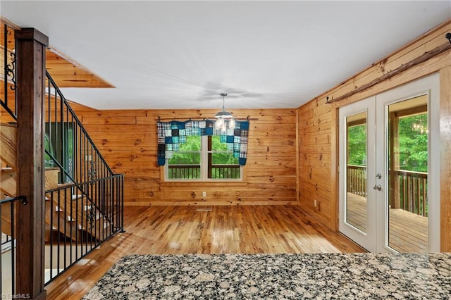 unfurnished room featuring an inviting chandelier, wood walls, french doors, and hardwood / wood-style flooring