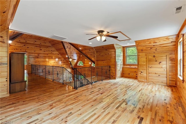 additional living space with wooden walls, a ceiling fan, wood finished floors, and visible vents