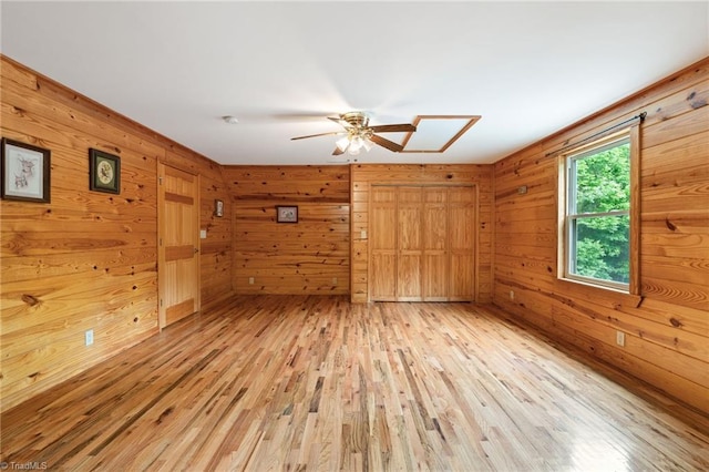 empty room with wooden walls, a ceiling fan, and light wood-style flooring