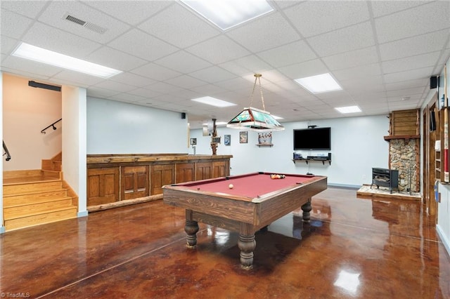 playroom featuring concrete flooring, visible vents, a paneled ceiling, and a wood stove
