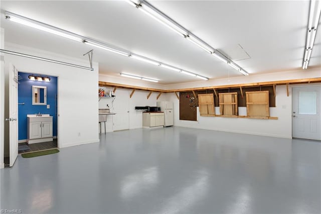 garage featuring baseboards, freestanding refrigerator, and a sink