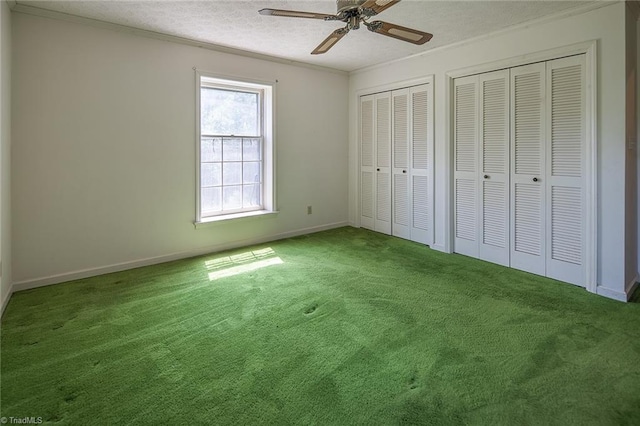 unfurnished bedroom with carpet flooring, ceiling fan, a textured ceiling, two closets, and ornamental molding